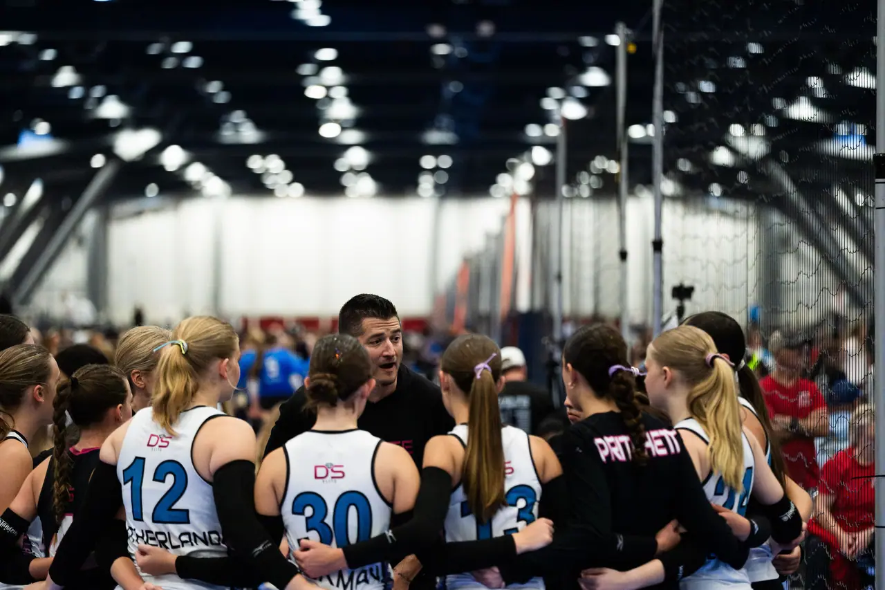 DS Elite coach in a club hoodie talking with his players in a tight huddle between sets