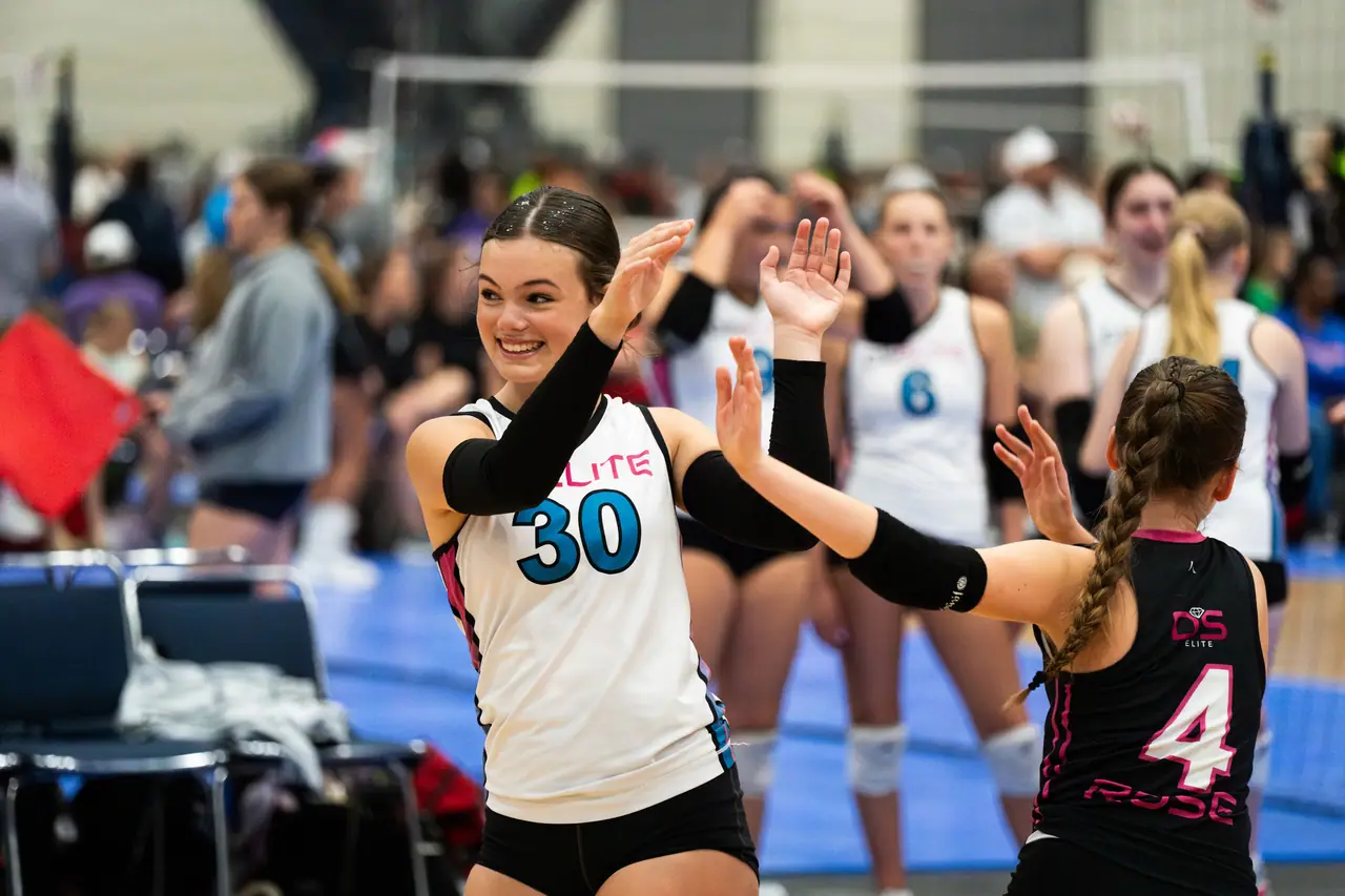 DS Elite player in a white uniform going in for a two-handed high five with the team libero