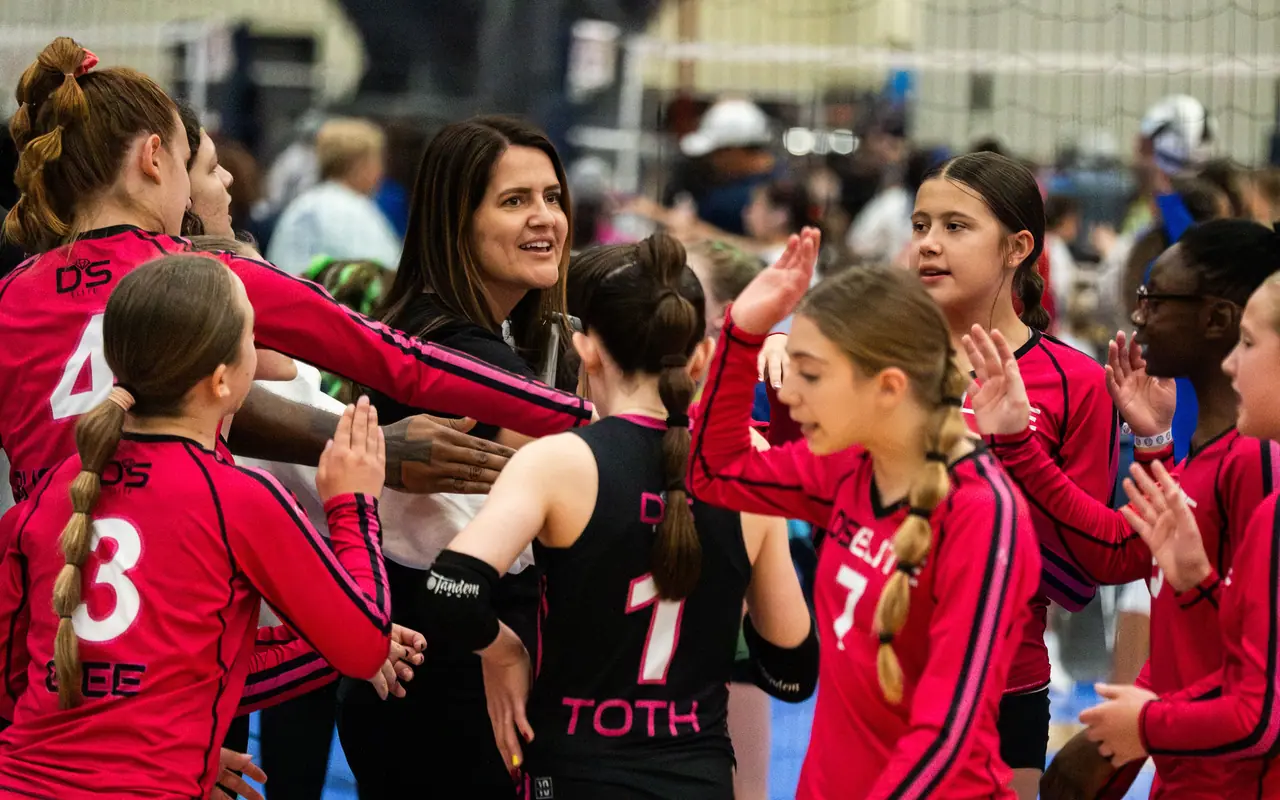 Smiling DS Elite coach surrounded by players high-fiving in a timeout huddle