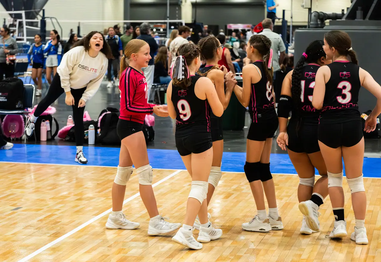 Younger DS Elite team in black uniforms high-fiving in a line while a staff member cheers behind them